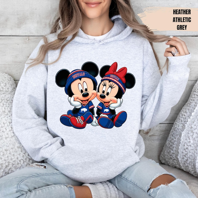 A woman wearing a grey hoodie with a graphic of two cartoon mice, one wearing a blue shirt and the other a red shirt, sitting together.