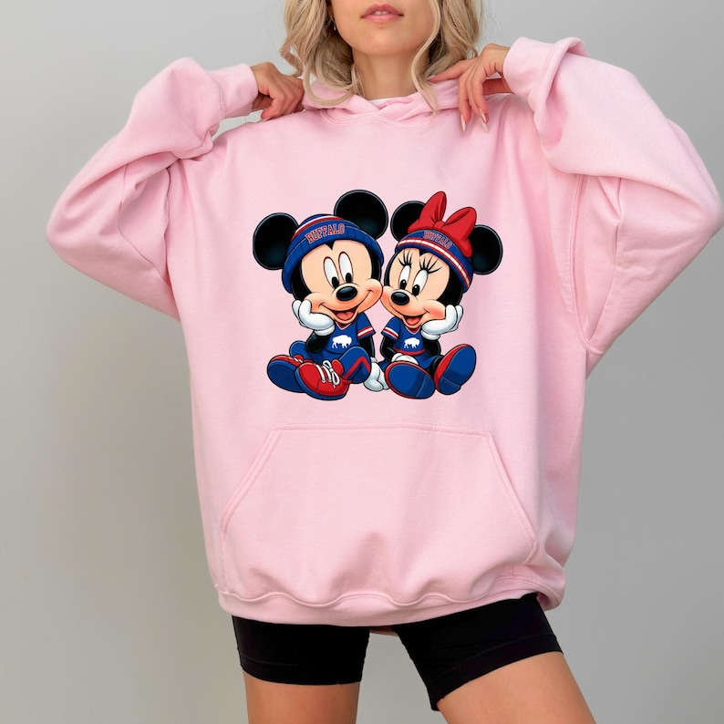 A woman wearing a pink hoodie with a graphic of two cartoon mice, Minnie Mouse and Mickey Mouse, sitting together.