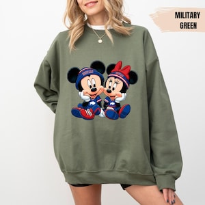 A woman wearing a green sweatshirt with a graphic of two cartoon mice, one male and one female, sitting together.