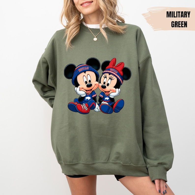 A woman wearing a green sweatshirt with a graphic of two cartoon mice, one male and one female, sitting together.