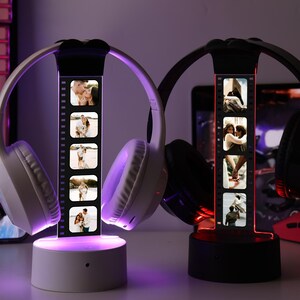 May include: Two illuminated headphone stands, one white and one black, each displaying a strip of photos. The white stand holds white headphones, the black stand holds black headphones. The stands emit a soft, colored glow, creating a warm ambiance.