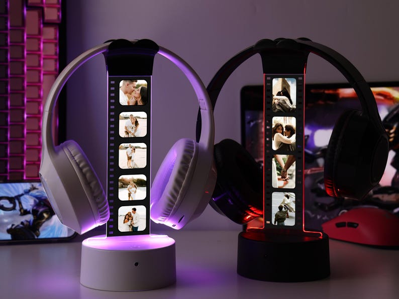 May include: Two illuminated headphone stands, one white and one black, each displaying a strip of photos. The white stand holds white headphones, the black stand holds black headphones. The stands emit a soft, colored glow, creating a warm ambiance.