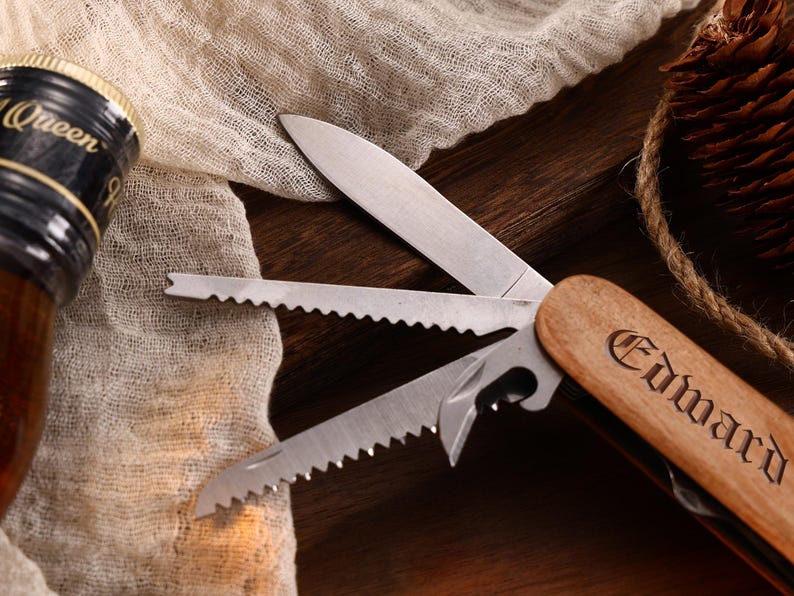 May include: Close-up of a multi-tool with a wooden handle engraved with the name "Edward". The tool has several open blades and a bottle opener. A bottle with a black and gold label is visible in the background.