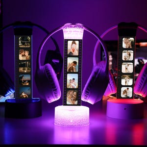 May include: Three personalized photo lamps with wireless headphones. Each lamp displays a strip of photos and sits on a base. The lamps are illuminated with purple and white light, creating a romantic ambiance. The headphones are white and purple.