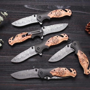 May include: Five folding pocket knives with Damascus steel blades, carbon fiber bolsters, and olive wood handles. Each handle features a unique engraved monogram and the word GROOMSMAN. One knife is partially folded, showing a metal pocket clip.