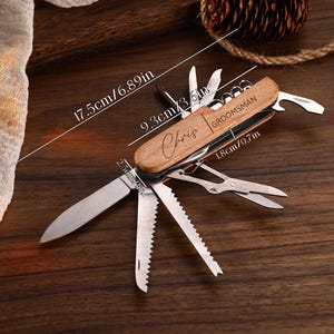 May include: A wooden-handled multi-tool knife with multiple blades and tools extended. The knife is 6.89 inches long and features the engraved name "Chris" and the word "Groomsman". The knife is on a dark wooden surface.