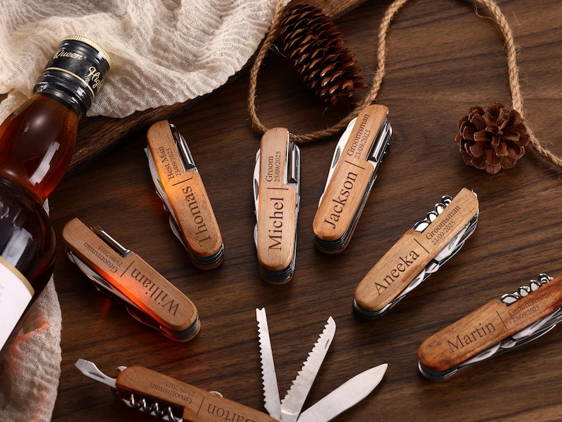 May include: A collection of personalized wooden pocket knives with various names and dates engraved on them. The knives are arranged on a dark wooden surface, alongside a bottle of liquor and decorative elements.