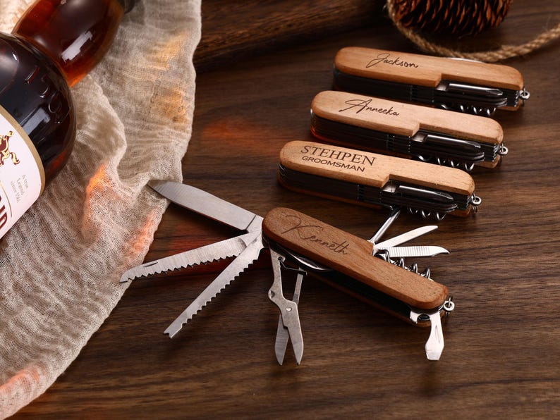 May include: A collection of personalized wooden multi-tools with various tools, including knives, corkscrews, and scissors. The tools are engraved with names and the word "Groomsman". The tools are displayed on a dark wooden surface.