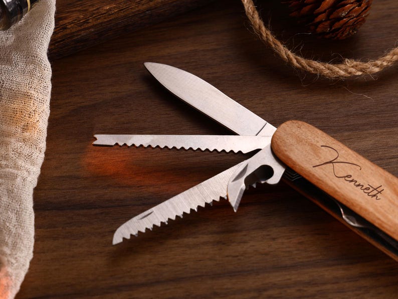 May include: A multi-tool with a wooden handle and stainless steel blades. The blades include a knife, saw, and bottle opener. The handle is engraved with the name "Kenneth". The tool is displayed on a dark wood surface.
