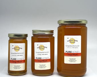 May include: Three glass jars of honey, labeled "Hungry Bear Farms", with the text "Pure Honey Orange Blossom" on the front. The jars are different sizes, with the largest jar being 2 pounds, the middle jar being 1 pound, and the smallest jar being 1/2 pound.