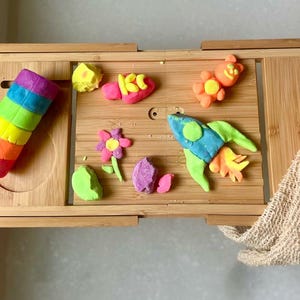 May include: A wooden tray with colorful play dough creations, including a rocket, a flower, a bear, and a fish. The play dough is arranged on a bamboo tray with a light brown background.