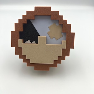 Könnte beinhalten: Ein brauner, pixelig gestalteter Rahmen mit einem beige-schwarzen Pixeldesign im Inneren. Das Design zeigt eine schwarze Bergform mit einer beigefarbenen Sonne und einer beigefarbenen Bergkette.