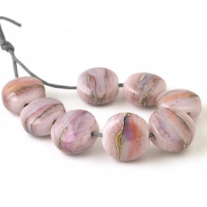 May include: A strand of pink and white glass beads with gold flecks. The beads are round and have a marbled appearance.