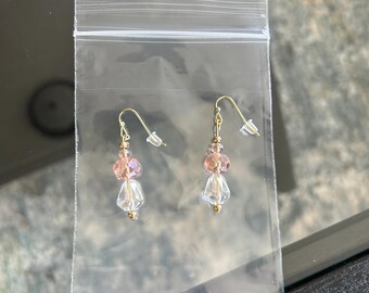 May include: A pair of dangle earrings with pink and clear glass beads and gold accents. The earrings are packaged in a clear plastic bag.