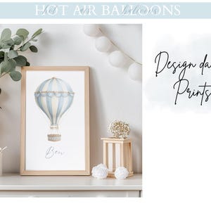 May include: A framed print with a watercolour illustration of a blue and white hot air balloon. The artwork is in a light wood frame and includes the name "Ben" at the bottom. The words "Design dainty Prints" are written in cursive.