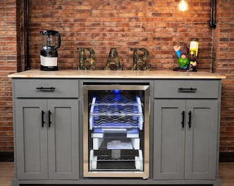 May include: A gray bar cabinet with a built-in wine cooler, wooden countertop, and gray cabinet doors. The word "BAR" is spelled out in gold letters. A blender and a gnome statue are on the countertop.