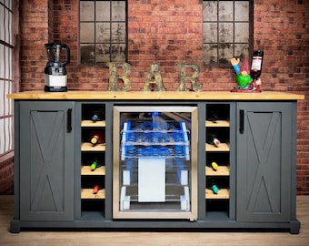 May include: A gray wooden bar cabinet with a light wood countertop and a built-in wine cooler. The cabinet has two doors with an X design and open shelves for wine bottles. The word "BAR" is displayed on the countertop.