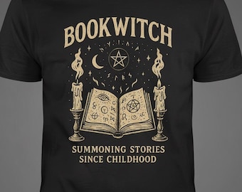 Op de afbeelding: Een zwart t-shirt met korte mouwen en een beige grafische print van een open boek met occulte symbolen, geflankeerd door twee brandende kaarsen. Boven het boek staat de tekst BOOKWITCH en daaronder de tekst SUMMONING STORIES SINCE CHILDHOOD.