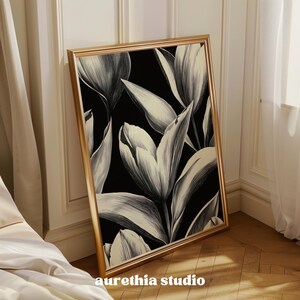 May include: A black and white floral print in a gold frame. The print features large, stylized tulips with a black background.