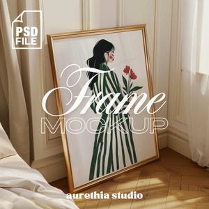 Puede incluir: Una maqueta de marco dorado con un fondo blanco y una ilustración colorida de una mujer con un vestido a rayas sosteniendo flores rojas. El texto "Frame Mockup" está escrito en una fuente estilizada debajo de la imagen. El texto "aurethia studio" está escrito en una fuente más pequeña debajo de la imagen.