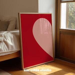 May include: A framed art print featuring a bold design of a heart shape. The artwork has a vibrant red background with a soft pink heart shape. The frame is a light wood color, and the text "aurethia studio" is at the bottom.