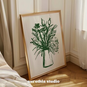 May include: A gold framed mirror with a green line drawing of a bouquet of flowers in a vase. The flowers are stylized and abstract.