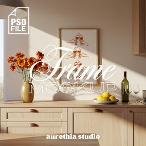 Puede incluir: Una escena de cocina con una impresión enmarcada que presenta un dibujo lineal de manos brindando con copas de vino. Un jarrón de flores naranjas, una botella de vino y limones en un cuenco están sobre la encimera de madera. El texto "Frame Mockup" está superpuesto.
