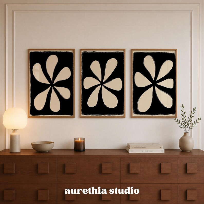 May include: Three rectangular wall art prints in light wood frames, each featuring a large, beige, six-petaled flower shape centered on a solid black background. The text "aurethia studio" is printed in white at the bottom center of the image.