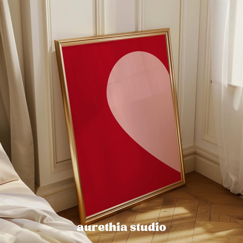 May include: A framed print with a red background and a pink heart shape in the center. The frame is gold.