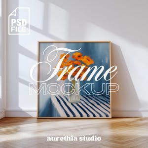 May include: A framed art print mockup featuring a painting of orange flowers in a vase on a striped table. The artwork is set against a blue backdrop. The words "Frame Mockup" are displayed on the artwork. The frame is made of wood.