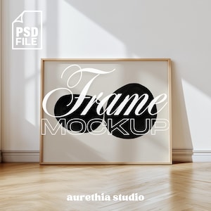 May include: A rectangular frame mockup with a light wood finish, displaying a minimalist design. The artwork features two large black circular shapes against a cream background. The word "Frame" is written in a decorative font, with "Mockup" below. The PSD file logo is in the upper left corner.