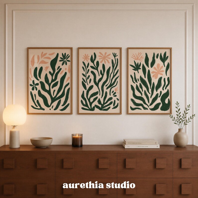 May include: A set of three vertical wall art prints in wooden frames, each featuring abstract botanical illustrations with dark green leaves and light pink flowers on a beige background. The text "aurethia studio" is printed in white at the bottom.
