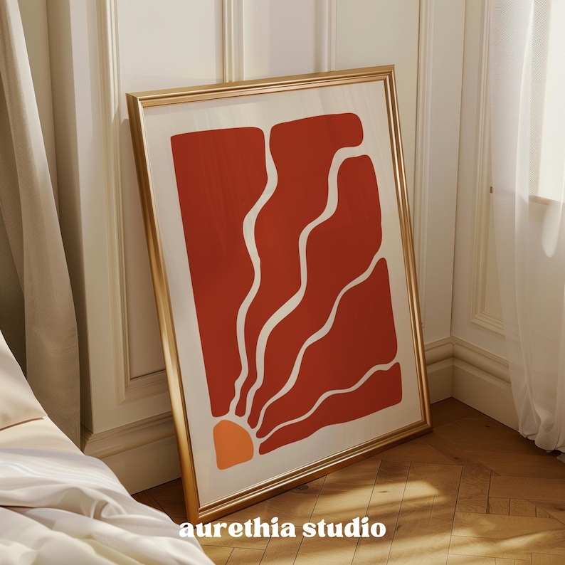 May include: A framed abstract art print with a red and white design. The design features a sunburst shape with curved lines radiating outward. The print is in a gold frame.