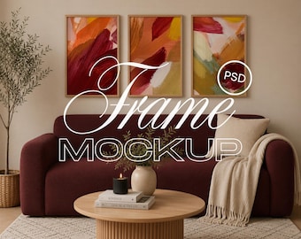 May include: Three vertical framed art prints with abstract brushstrokes in shades of red, orange, and yellow hanging above a dark red sofa. A round wooden coffee table with a black candle and books sits in front of the sofa. Text reads Frame MOCKUP.