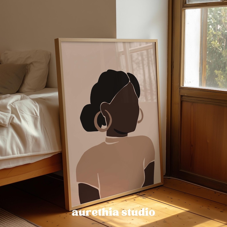 May include: A framed art print featuring a minimalist illustration of a woman. The artwork depicts a woman with dark skin, black hair in a bun, and large hoop earrings. The color palette includes shades of brown, beige, and black. The text "aurethia studio" is at the bottom.