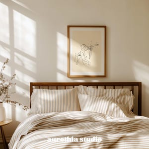 May include: A bedroom scene featuring a wooden bed frame, striped bedding, and a framed art print. The art print displays a minimalist line drawing of two figures. The text "aurethia studio" is visible on the bedding.
