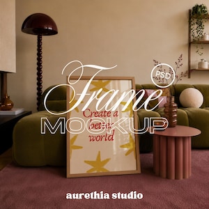 May include: A rectangular wooden picture frame containing a white print with yellow star illustrations and the red text Create a better world. The frame is positioned on a dark pink rug in front of a green sofa, a round pink side table, and a lamp.