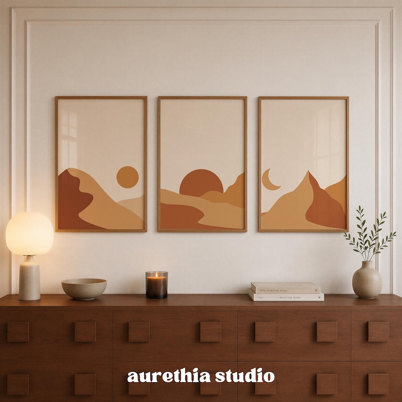 May include: Three rectangular wall art prints featuring abstract desert landscapes in shades of terracotta, burnt orange, and beige. The left print shows a sun, the center a large sun, and the right a crescent moon over layered mountain silhouettes.