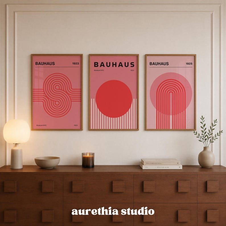 May include: Three framed wall art prints featuring Bauhaus designs in shades of pink and red. The left print shows a linear S-shape, the center a solid red circle, and the right a series of concentric arches. Each print includes the text Bauhaus.