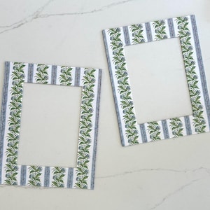 May include: Two white picture frames with a blue and green floral pattern. The frames are empty.