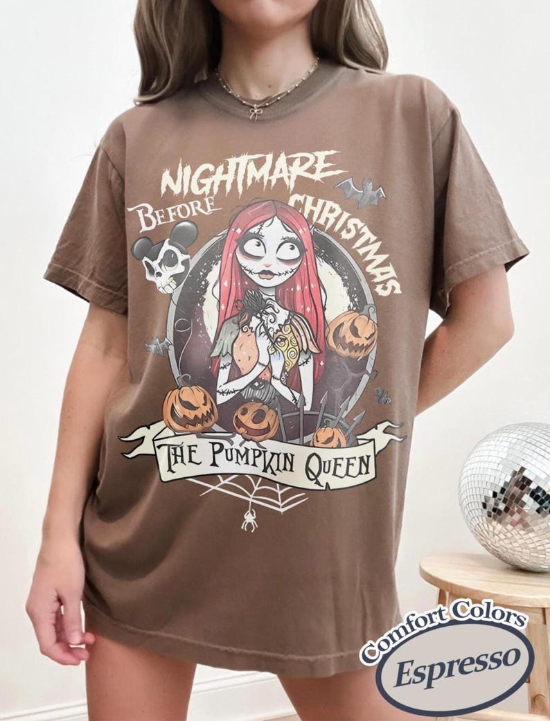 May include: Espresso-colored t-shirt featuring a graphic from "The Nightmare Before Christmas." The design includes Sally, pumpkins, and the text "The Pumpkin Queen." The shirt is a Comfort Colors brand.