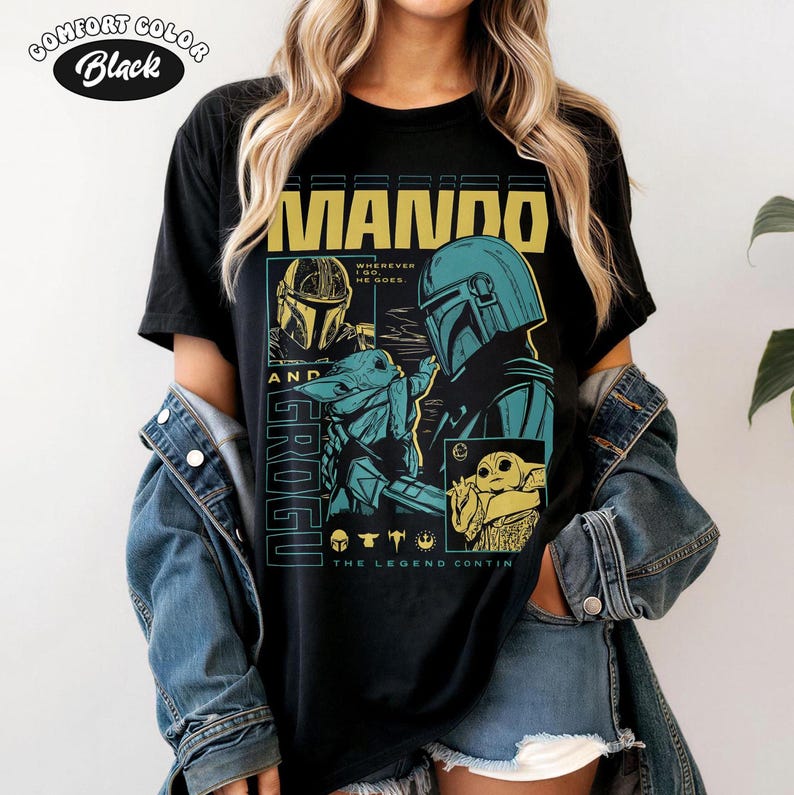 Pode incluir: Camiseta preta com um design gr&aacute;fico com o texto "MANDO AND GROGU". O design inclui ilustra&ccedil;&otilde;es de personagens da s&eacute;rie Star Wars, com detalhes turquesa e amarelo. O texto "THE LEGEND CONTINUES" tamb&eacute;m est&aacute; presente.