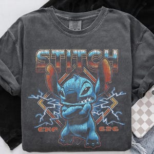 Peut inclure: T-shirt &agrave; manches longues gris fonc&eacute; avec un motif vieilli de Stitch, le mot "STITCH" au-dessus et "626" en dessous. Le personnage bleu Stitch a les bras crois&eacute;s et est entour&eacute; d'&eacute;clairs. Le t-shirt a un aspect vintage et us&eacute;.