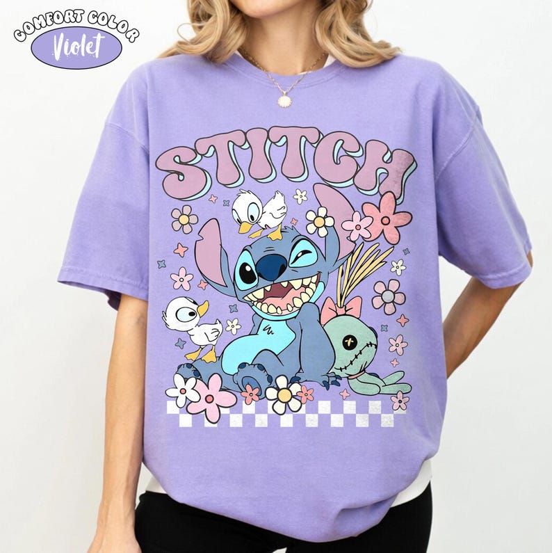May include: A violet Comfort Colors t-shirt with a graphic of Stitch from Lilo & Stitch. The design includes the word "Stitch" in pink bubble letters, Stitch, flowers, and ducks. The shirt has a relaxed fit.
