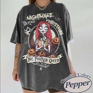 May include: Dark gray t-shirt featuring a graphic from "The Nightmare Before Christmas." The design includes Sally, pumpkins, and the text "The Pumpkin Queen." The shirt is from Comfort Colors, Pepper.