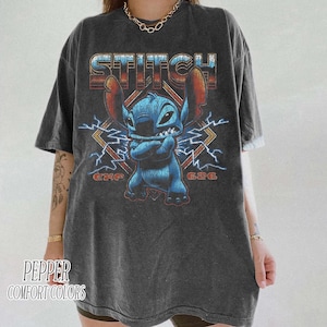 Peut inclure: T-shirt gris fonc&eacute; avec un personnage de dessin anim&eacute; bleu et le mot "STITCH" dans une police r&eacute;tro. Le motif comprend des &eacute;clairs et le texte "G24G" et "G36G".