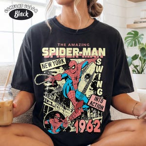 Puede incluir: Camiseta negra Comfort Colors con un gr&aacute;fico de Spider-Man. El dise&ntilde;o incluye el texto "THE AMAZING SPIDER-MAN NEW YORK SWING INTO ACTION 1962". La camiseta tiene un estilo de c&oacute;mic vintage.