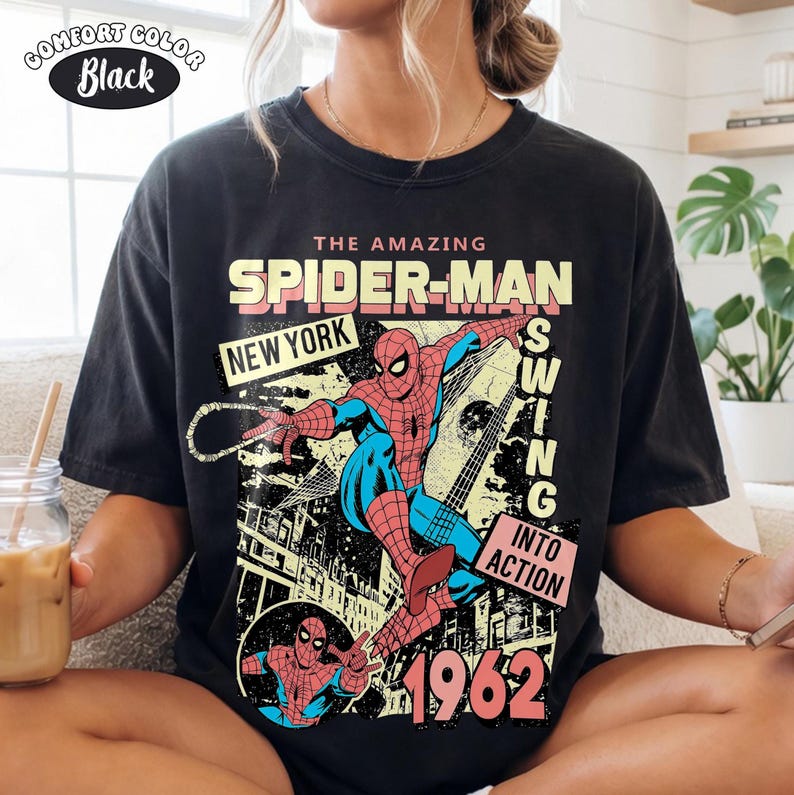 Puede incluir: Camiseta negra Comfort Colors con un gr&aacute;fico de Spider-Man. El dise&ntilde;o incluye el texto "THE AMAZING SPIDER-MAN NEW YORK SWING INTO ACTION 1962". La camiseta tiene un estilo de c&oacute;mic vintage.