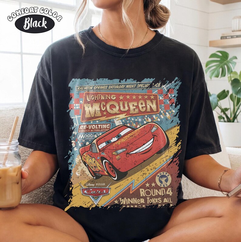 May include: Black Comfort Colors t-shirt with a Lightning McQueen graphic from Disney Pixar's Cars. The design includes McQueen, text, and a race theme. The shirt has a vintage, distressed appearance.