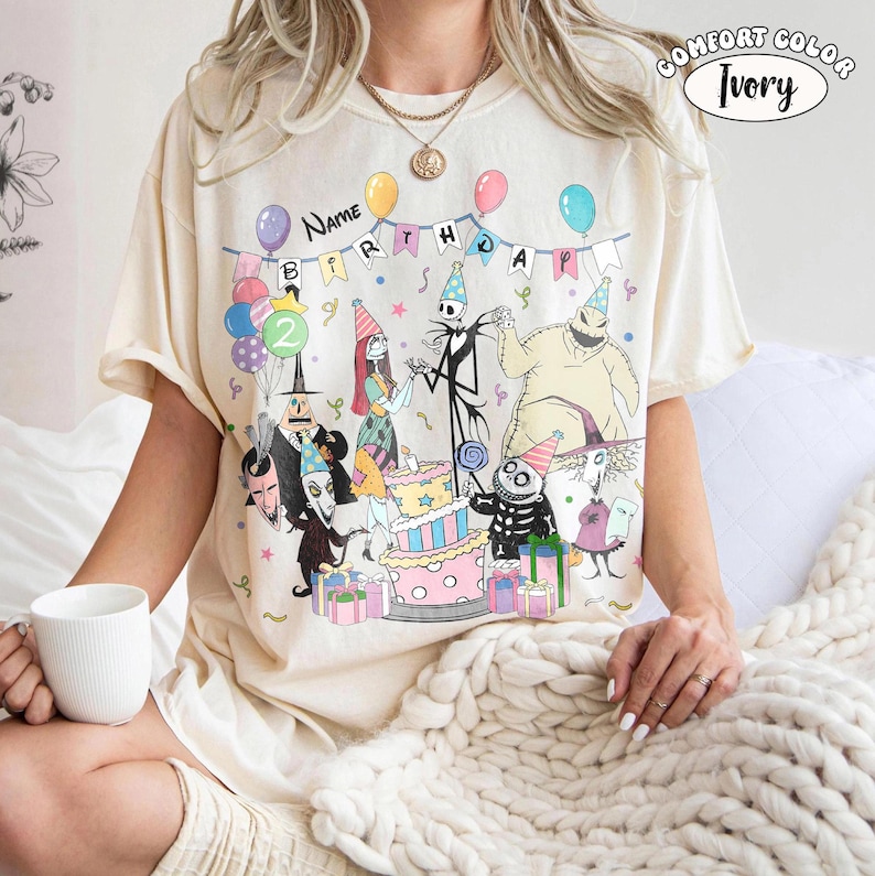 Op de afbeelding: Ivoor kleurig T-shirt met een verjaardagsfeestje met personages uit The Nightmare Before Christmas. Het ontwerp bevat een taart, ballonnen en de tekst "Name Birthday". Het shirt is gelabeld "Comfort Color Ivory".